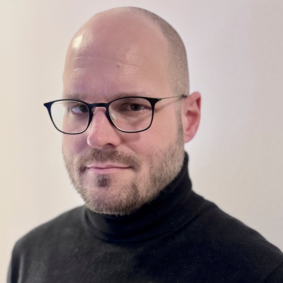 Falko Melz mit schwarzer Brille, kurzem Bart und schwarzem Rollkragenpullover, zur Kamera blickend